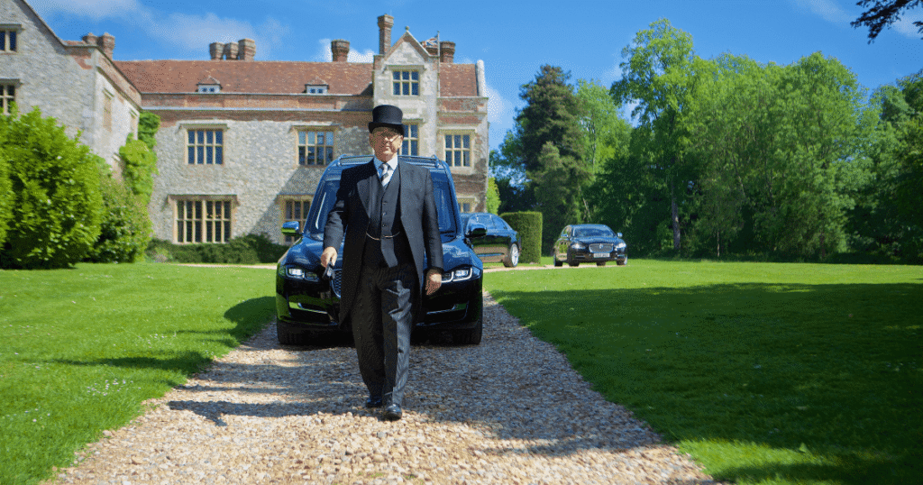 Funeral Director with top hat walking in front of parade of funeral cars