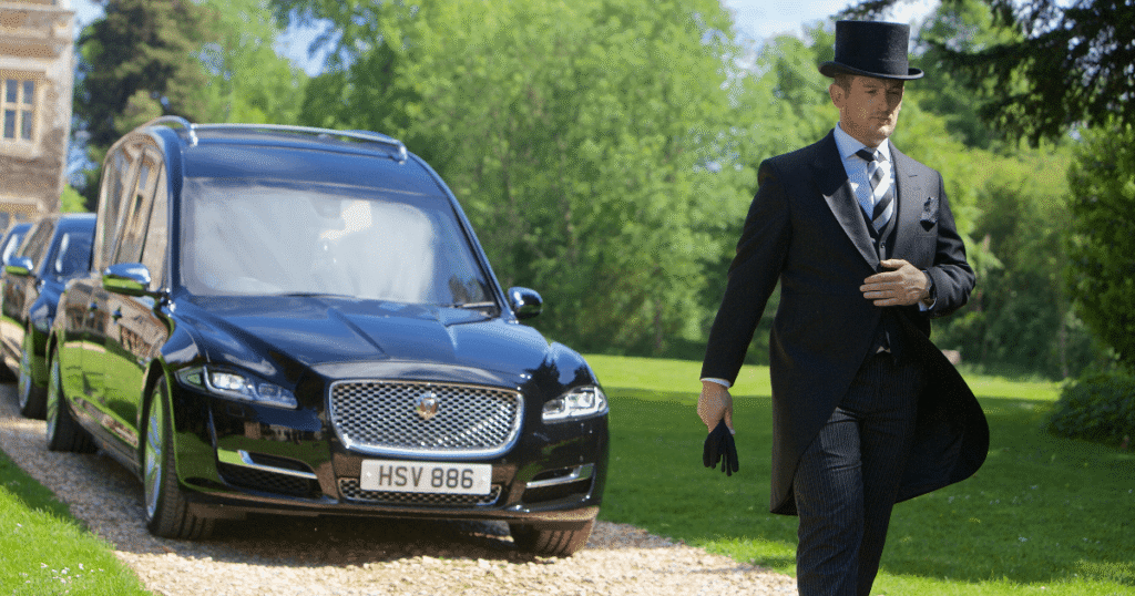 Funeral Director walking in front of hearse and limousines =