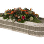 The Seagrass Coffin with large mixed orange flower spray on top
