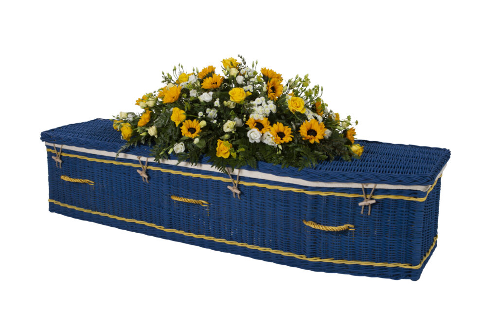 The Somerset Willow Colours Coffin in blue with yellow and white flower spray on top