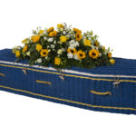The Somerset Willow Colours Coffin in blue with yellow and white flower spray on top